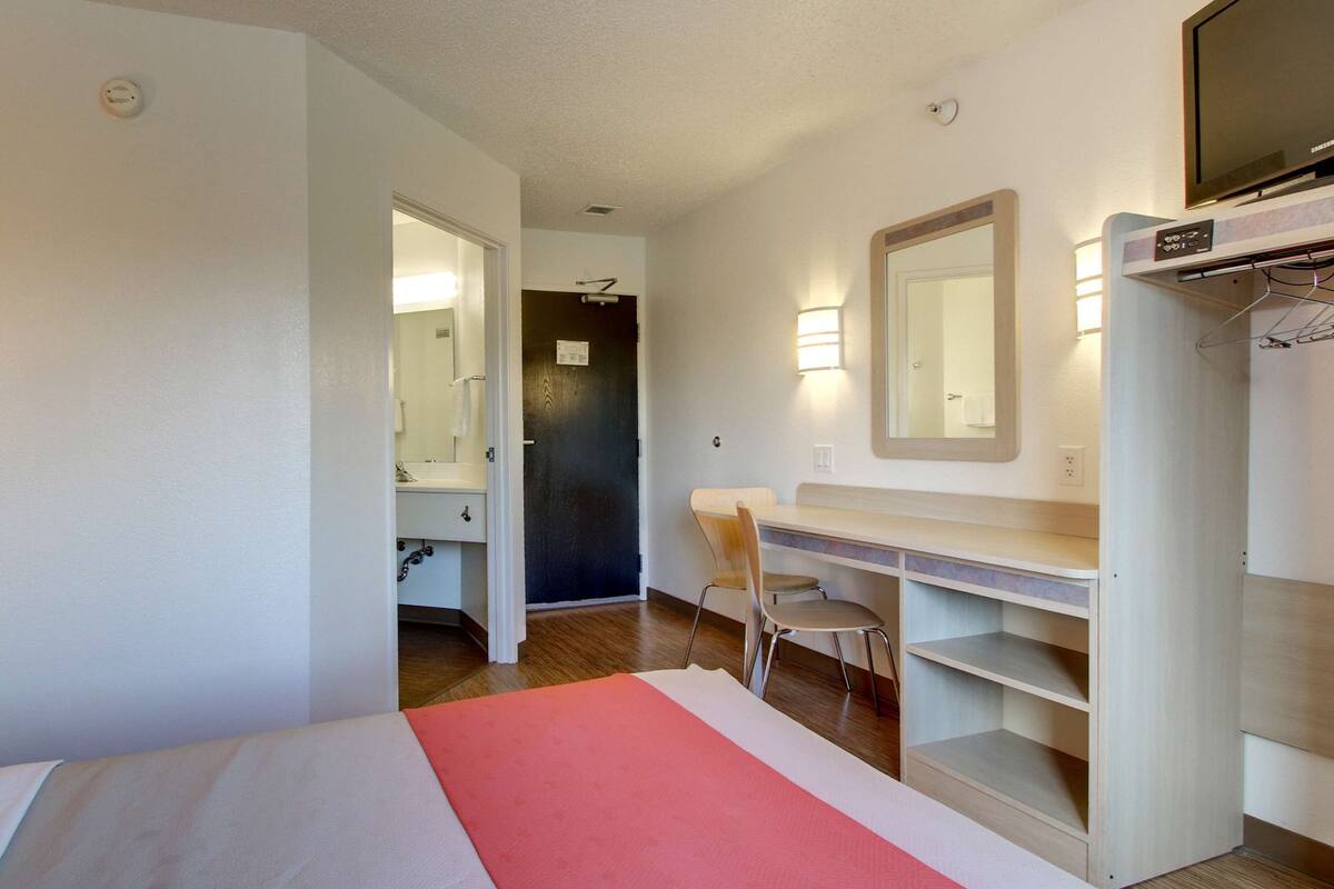 A hotel room with a bed, a desk with a chair, a mirror, and a wardrobe.