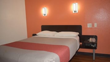A hotel room with a bed, two wall-mounted lights, a bedside table with a phone, and a red and white bedspread.