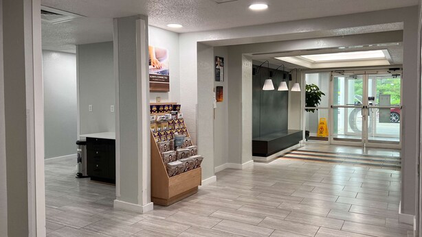 A modern lobby with a reception desk, a magazine rack, and a glass door leading outside. - Motel 6 Springfield, IL (Springfield)