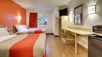 A hotel room with two beds, a desk, a chair, a TV, and a window with curtains.