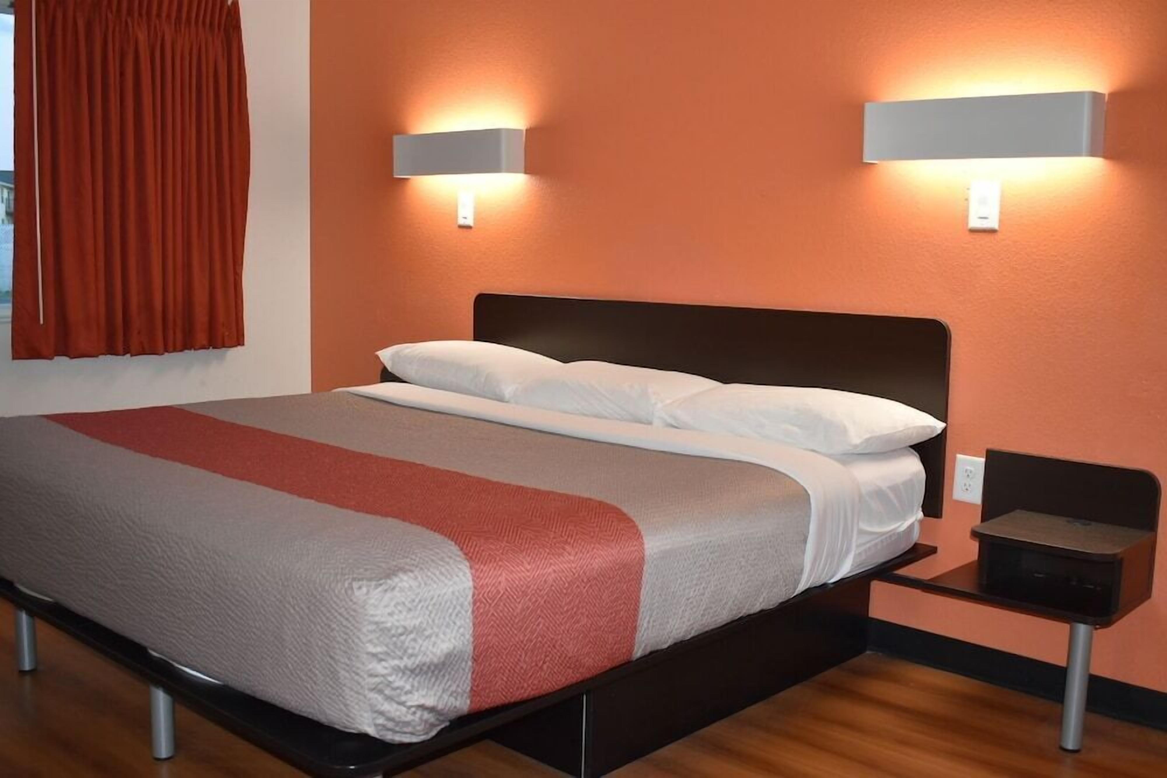 A hotel room with a bed, two wall-mounted lights, a nightstand, and a window with curtains.