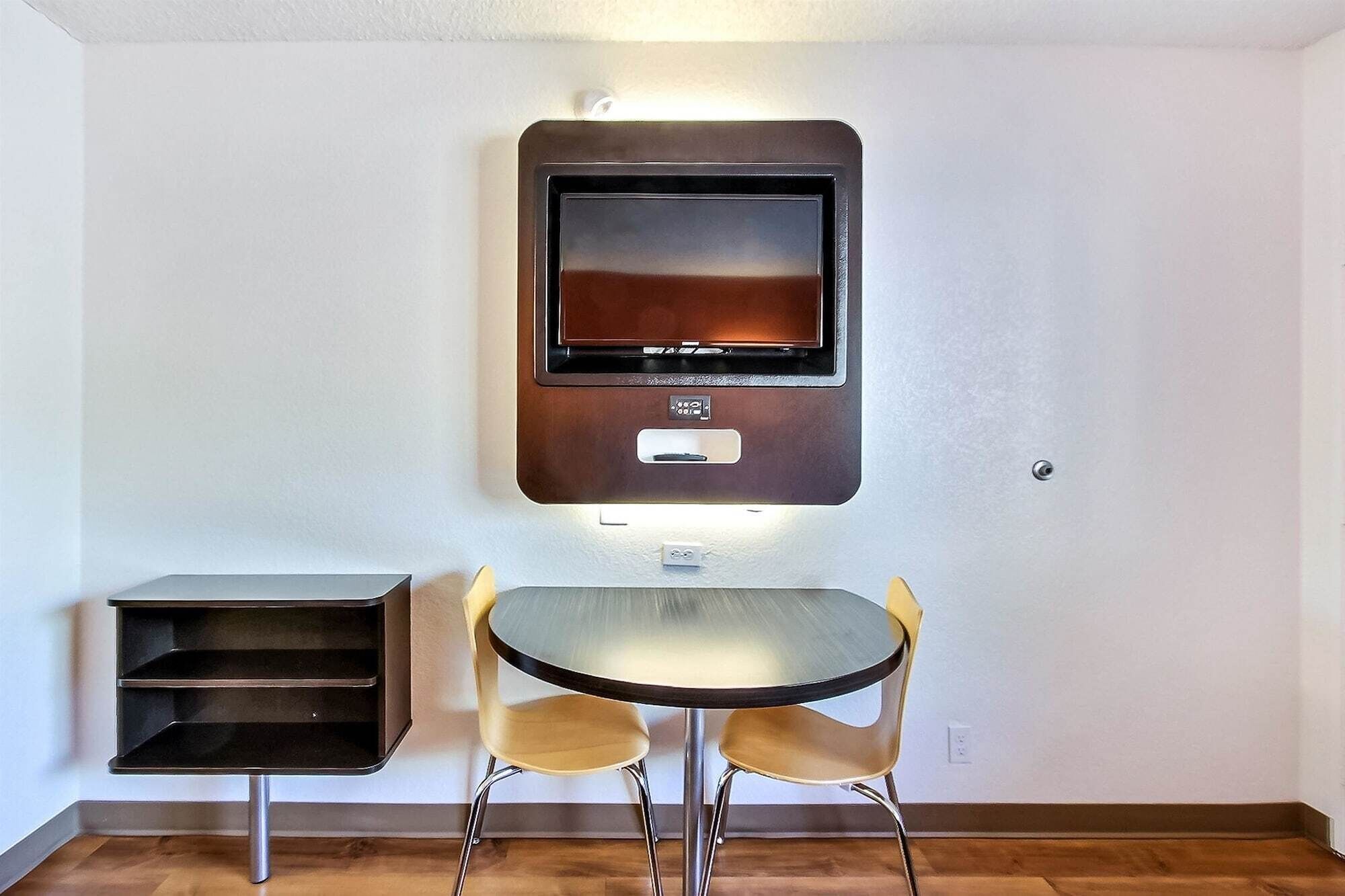 A compact room with a wall-mounted TV, a small table, and two chairs.
