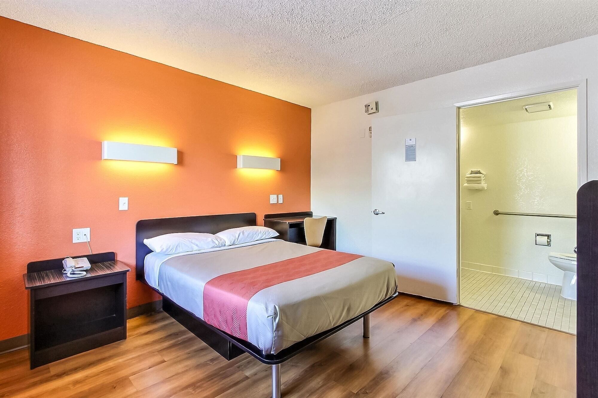 A hotel room with a bed, nightstands, a desk, a chair, and a bathroom with a toilet and shower.