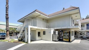 A two-story building with a white exterior, a red-tiled roof, and a small outdoor seating area with a vending machine. - Motel 6 Campbell, CA - San Jose (Campbell)