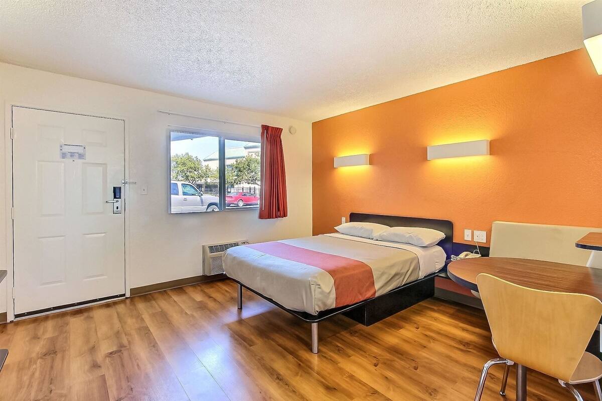 A hotel room with a bed, a desk, and a chair. There is a window with a view of the outside.