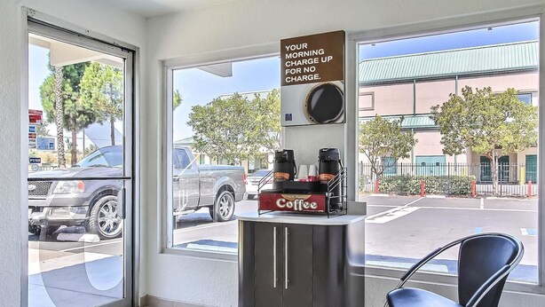 A coffee shop interior with a coffee station, a chair, and a view of the street outside. - Motel 6 Campbell, CA - San Jose (Campbell)