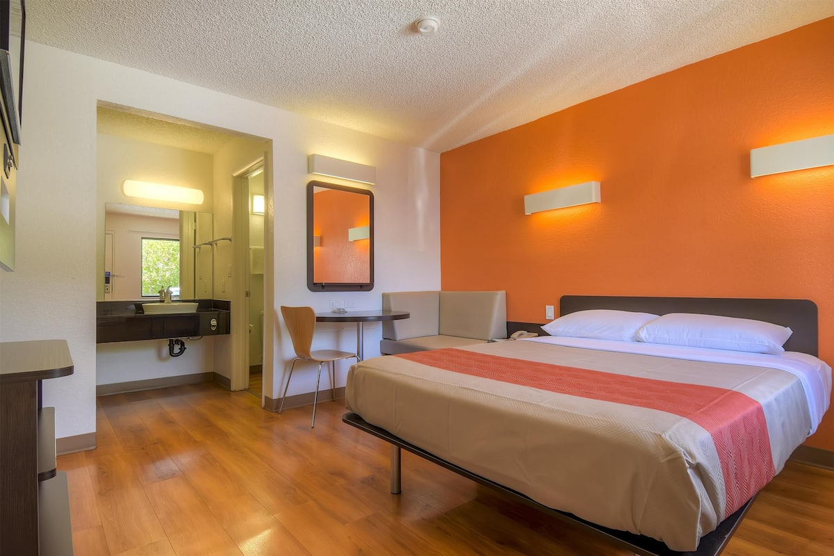 A hotel room with a bed, a desk, a chair, and a bathroom visible through an open door.