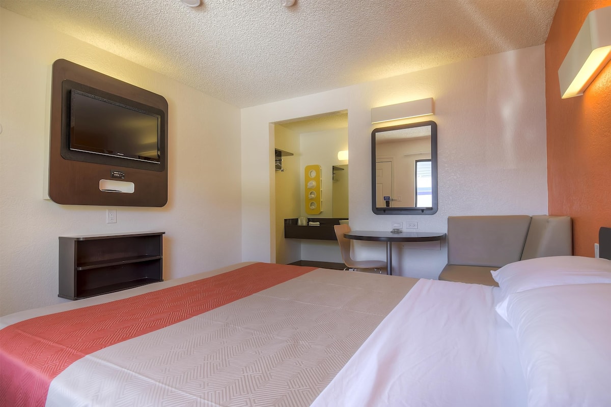 A hotel room with a large bed, a desk, a chair, a TV, and a mirror.