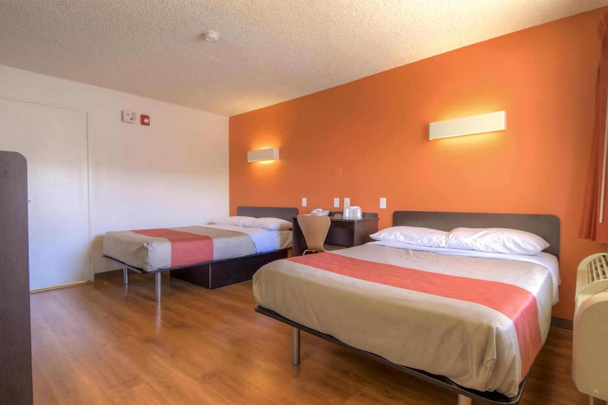 A hotel room with two single beds, a wooden floor, a white door, and a red wall.