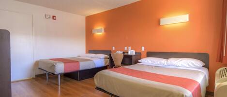 A hotel room with two single beds, a wooden floor, a white door, and a red wall.