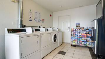 A laundry area with stacked washers and dryers, a fire alarm, and a refrigerator with magazines.