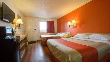 A hotel room with two beds, a TV, a desk, and a window with curtains.