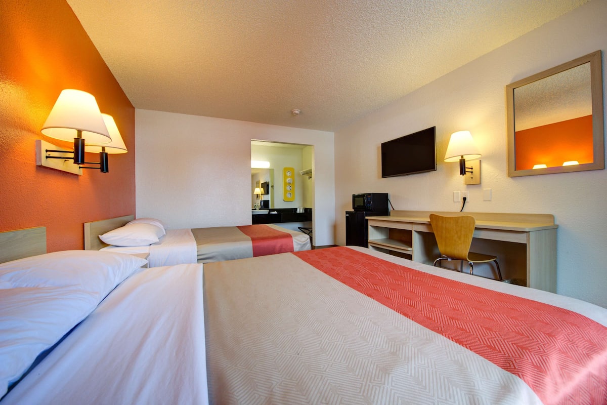 A hotel room with two beds, a desk, a chair, a TV, and a mirror.