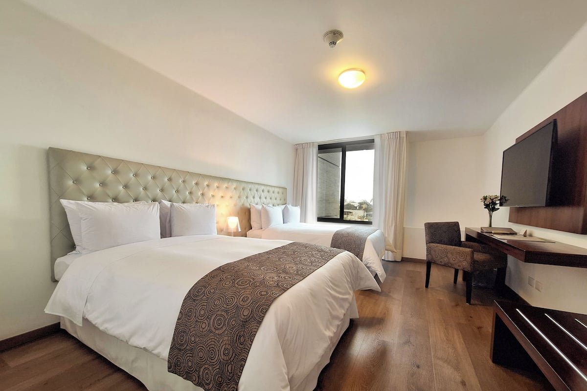 A hotel room with two beds, a desk, a chair, a TV, and a window with curtains.