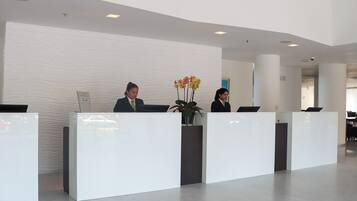 A reception area with two receptionists at white counters, a modern interior design, and a plant with yellow flowers.