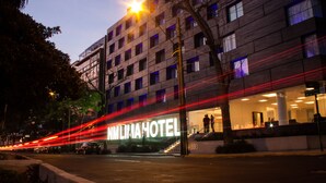 A modern hotel with a prominent sign, a well-lit entrance, and a visible staircase leading to the lobby. - NM Lima Hotel (Lima)