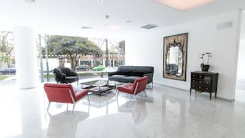 Eine großzügige Lobby mit modernem Design, ausgestattet mit einem schwarzen Ledersofa, roten Sessel, einem Couchtisch und einem großen Spiegel an der Wand.
