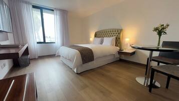 A hotel room with a bed, bedside table, lamp, chair, and a desk with a chair.