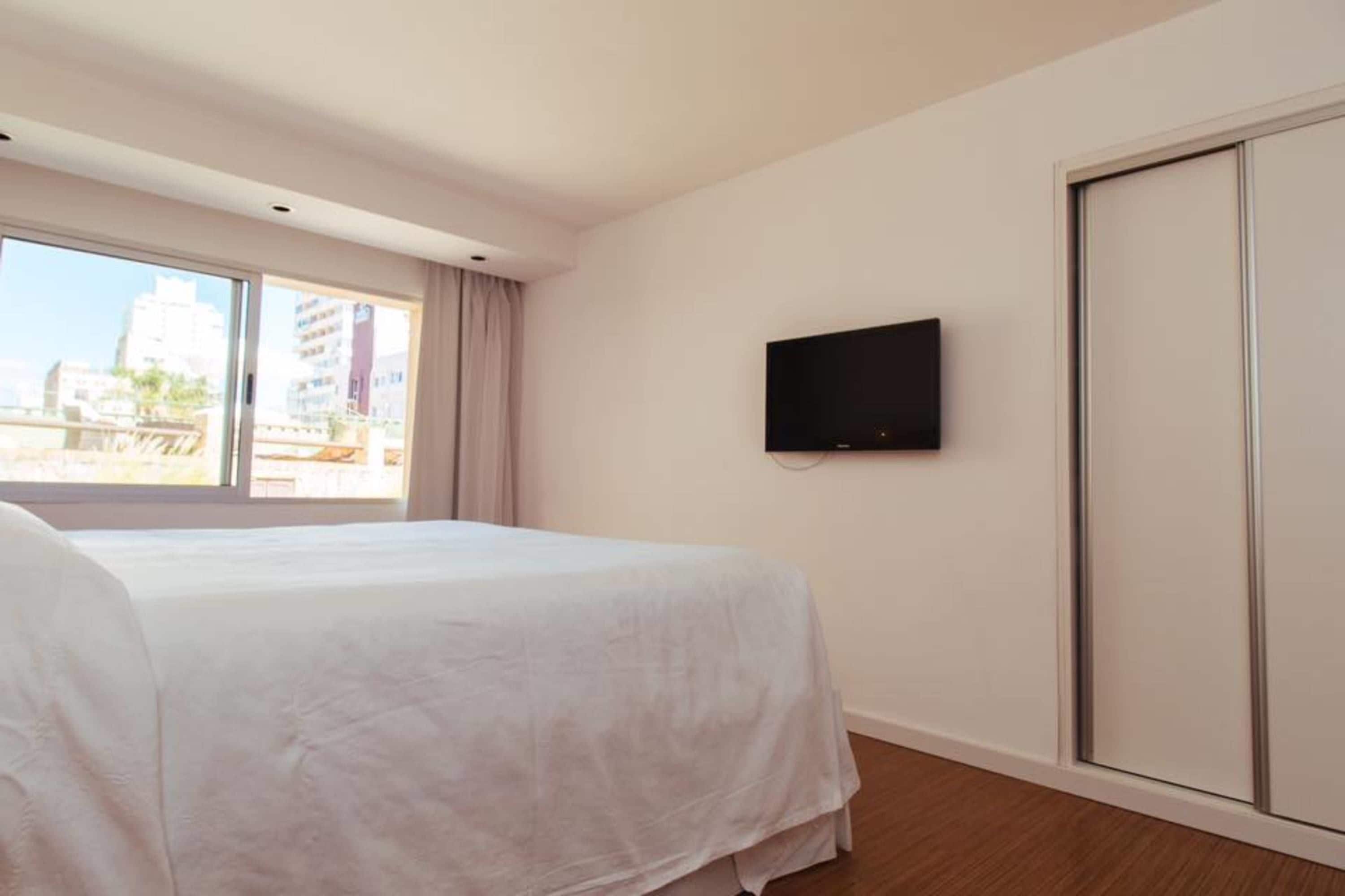 A hotel room with a bed, a TV mounted on the wall, and a sliding door.