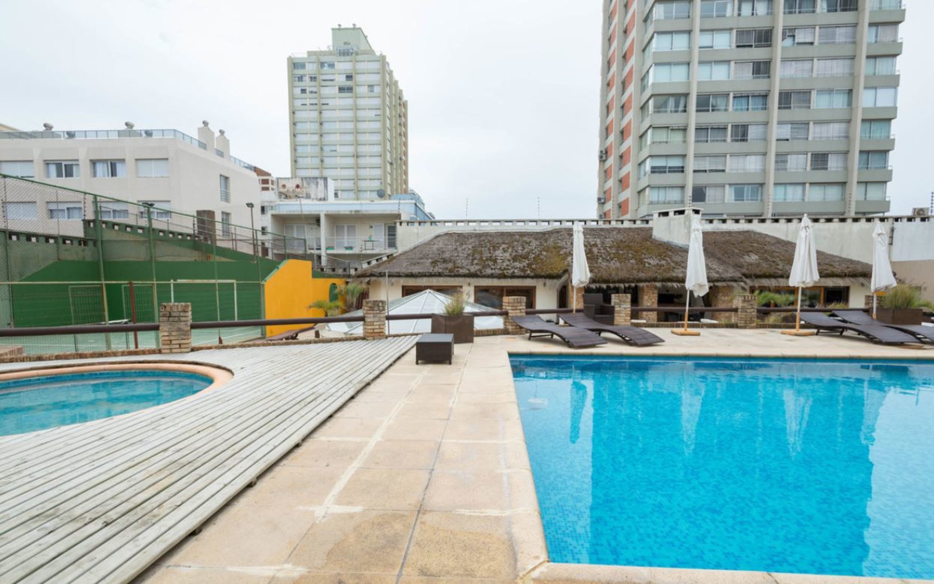 A rooftop pool area with lounge chairs and umbrellas, surrounded by high-rise buildings.