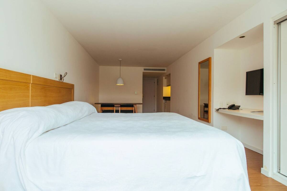 Una habitación de hotel con una cama, un escritorio, un espejo, un televisor y una puerta.