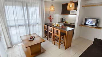 Una sala moderna con una mesa de comedor de madera, un sofá, una zona de cocina con microondas y un televisor.
