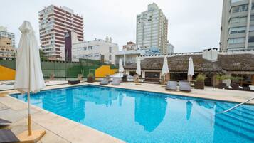 Una piscina techada, una piscina al aire libre, sombrillas