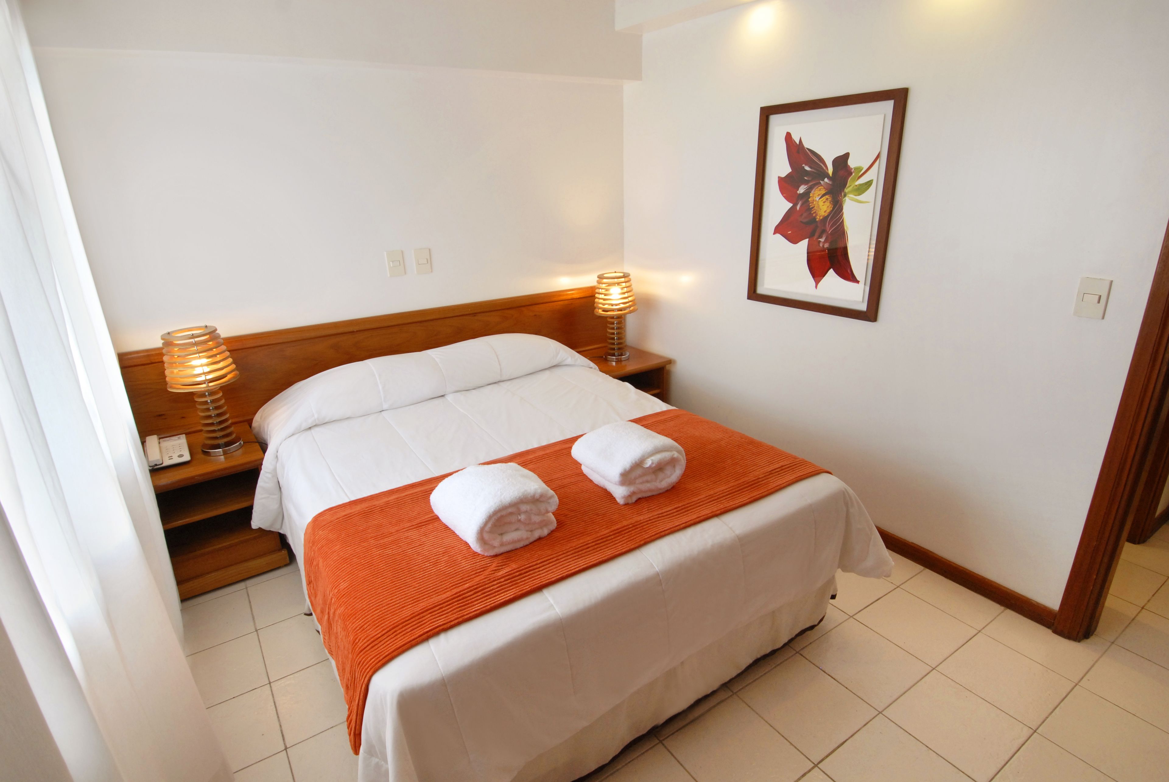 Habitación de hotel con una cama grande, dos lámparas de noche, una obra de arte enmarcada en la pared y un teléfono en la mesita de noche.