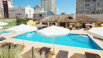 Una piscina techada, una piscina al aire libre, sombrillas