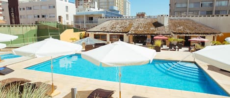 Una piscina techada, una piscina al aire libre, sombrillas