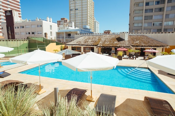 Una piscina techada, una piscina al aire libre, sombrillas