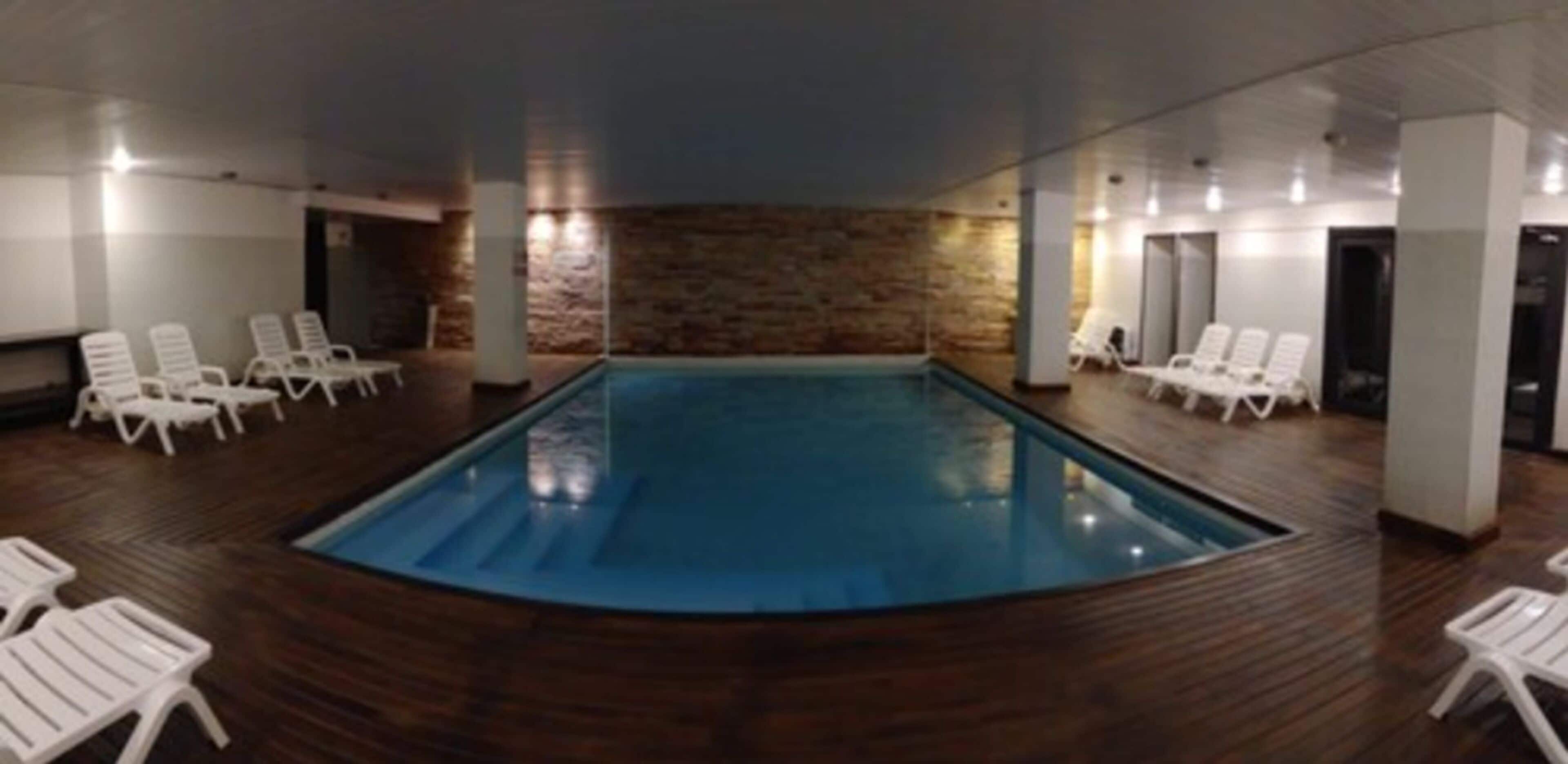 An indoor swimming pool with white lounge chairs and a stone wall backdrop.