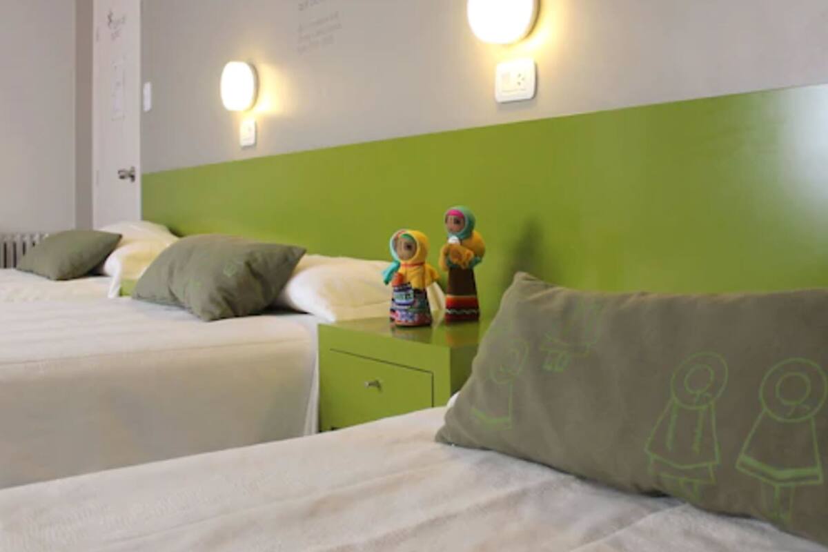 A hotel room with two beds, a green headboard, and wall-mounted lights.