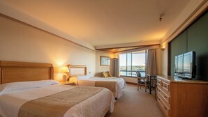 A hotel room with two beds, a desk, a chair, a dresser, and a television. - Hotel Marina Villa del Rio (Valdivia)
