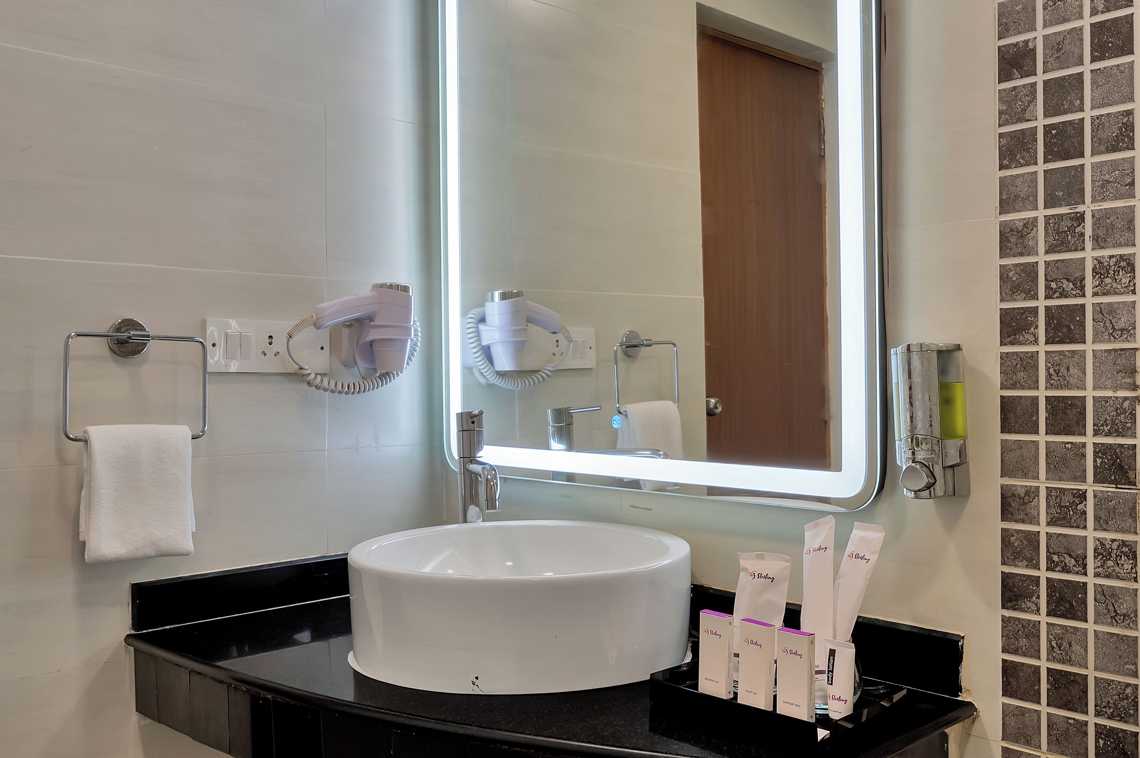 A bathroom with a large mirror, a white sink, and toiletries.