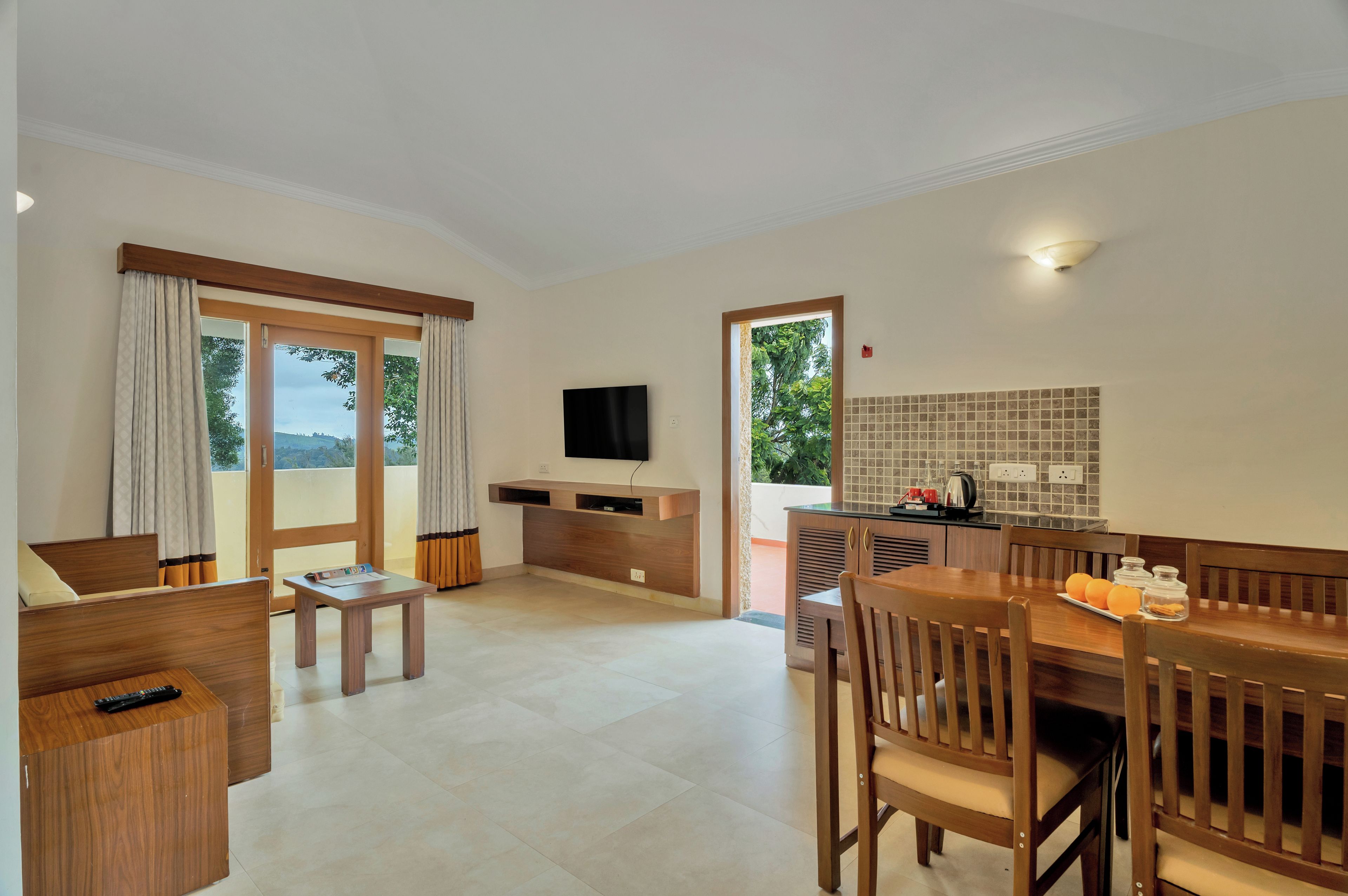 Habitación de hotel con zona de comedor, televisor montado en la pared y cocina con salpicadero de azulejos.