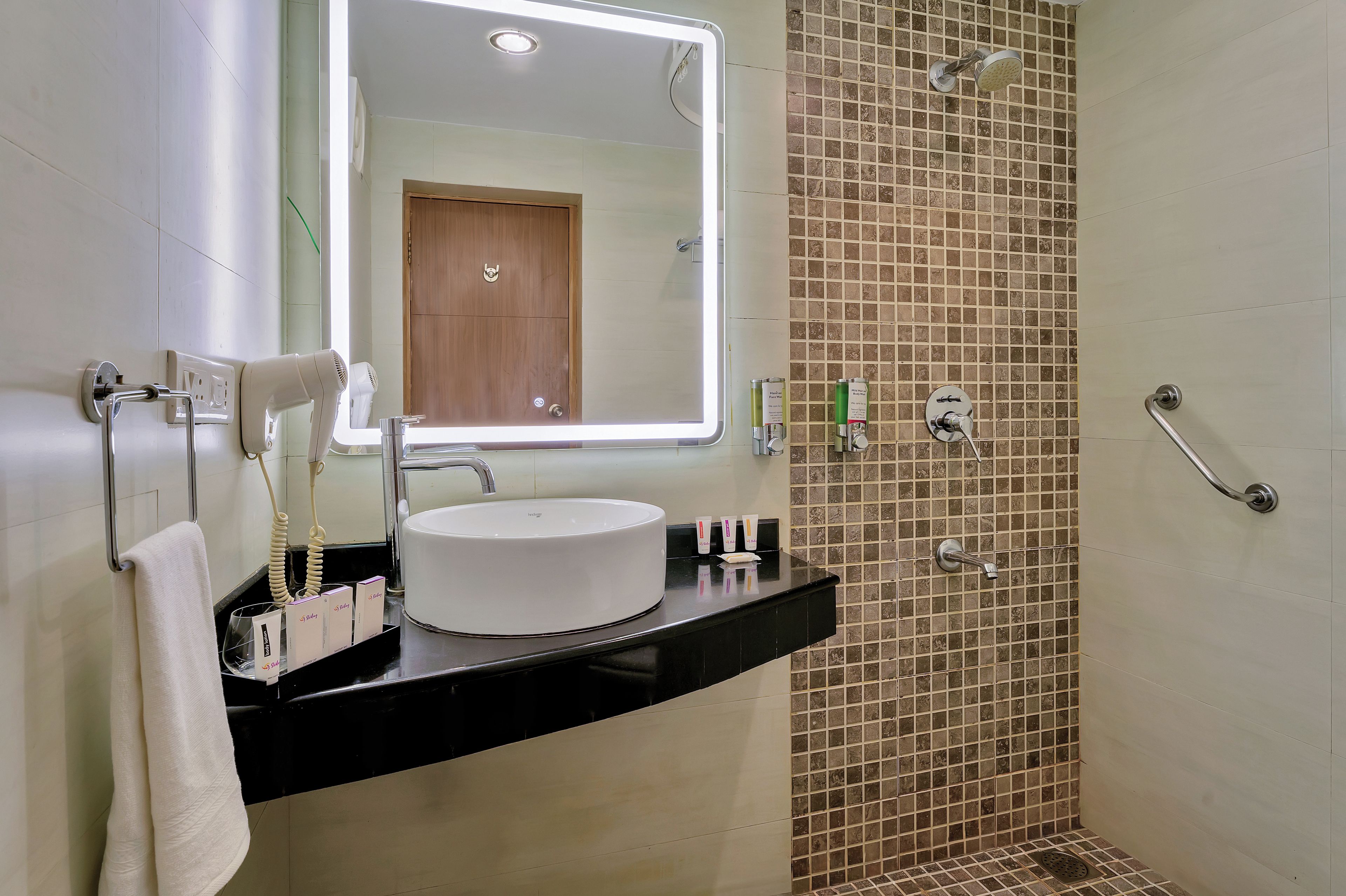 A bathroom with a round sink, a mirror, a towel rack, a handheld showerhead, and a shower with a tiled wall.