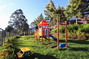 Un parque infantil con un tobogán, un columpio y una estructura roja para escalar.