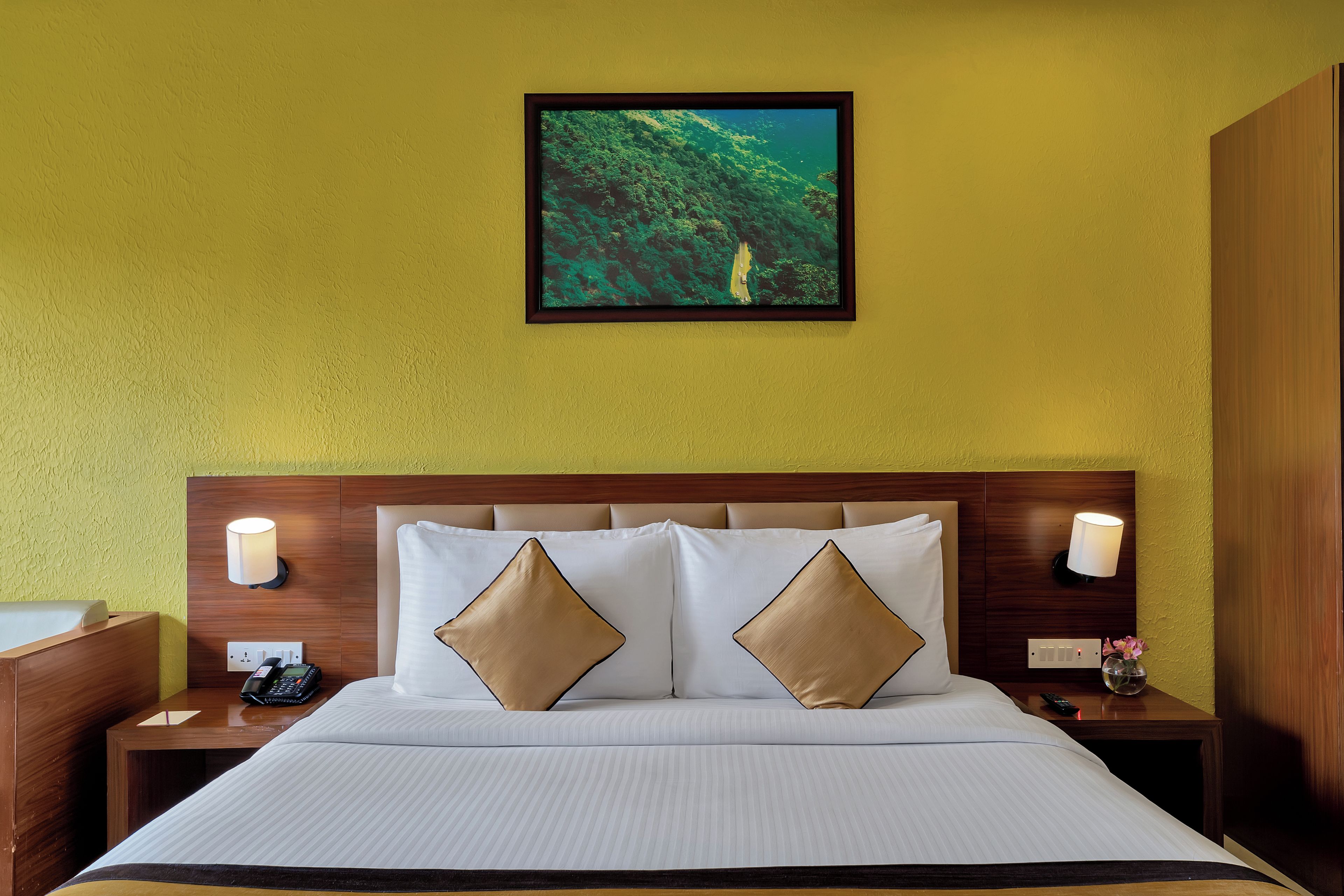 Habitación de hotel con cama, dos lámparas de noche, mesita de noche con teléfono y un cuadro en la pared.