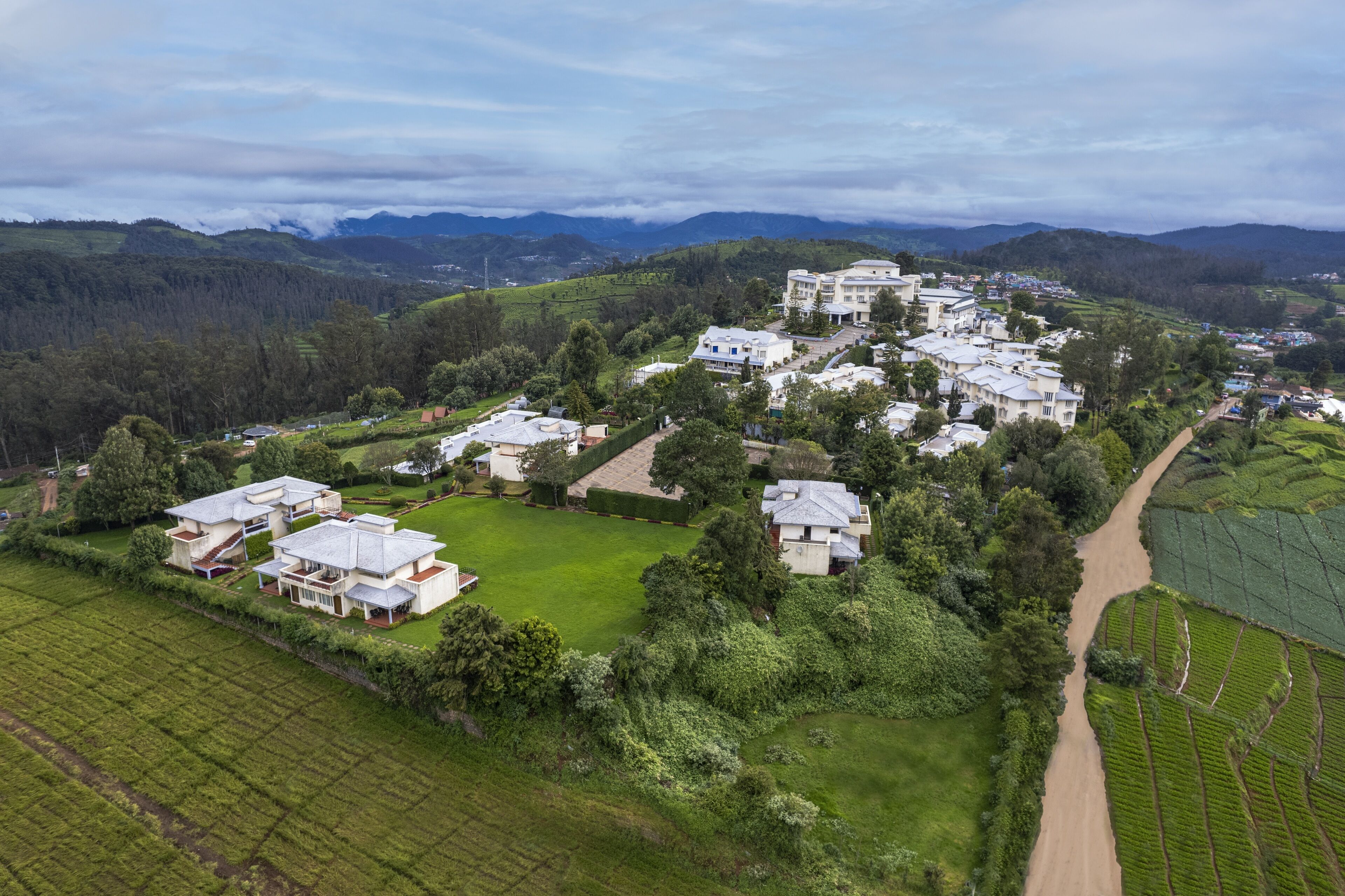 A residential area with multiple houses and a central building, surrounded by green fields and hills.