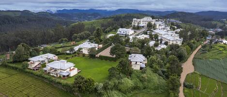 A residential area with multiple houses and a central building, surrounded by green fields and hills.