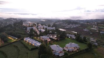 Vista aérea de una zona residencial con varias casas y un edificio grande, rodeada de campos verdes y un paisaje montañoso.