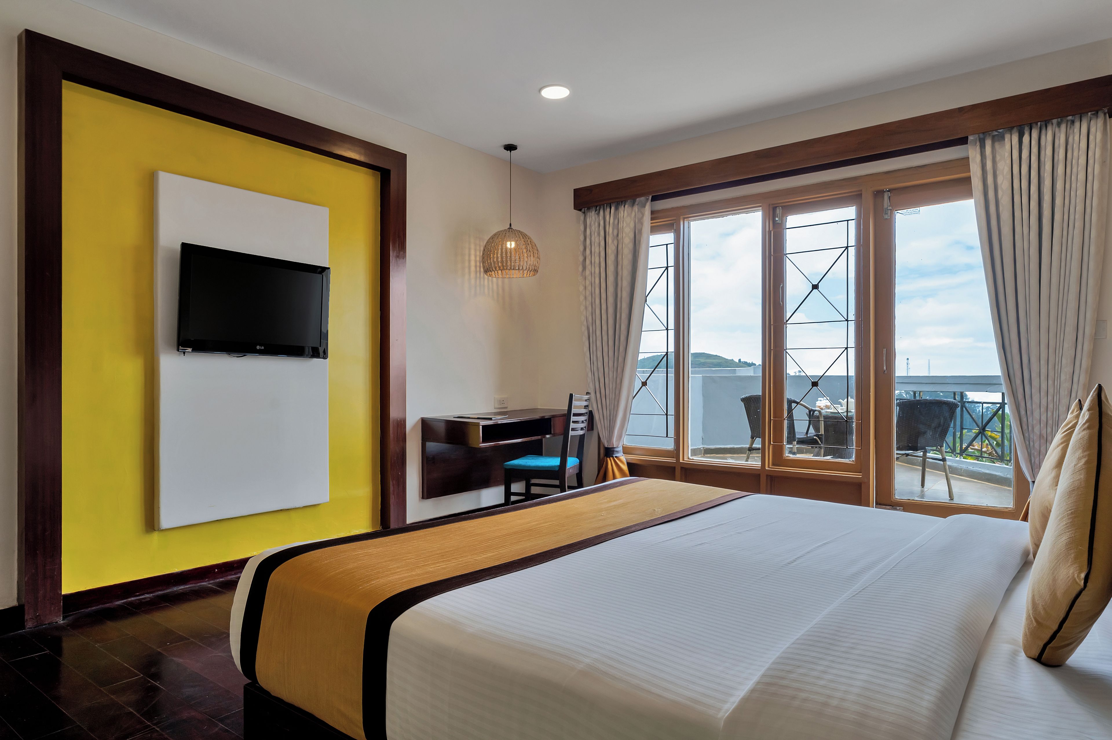 A hotel room with a bed, a desk, a TV mounted on the wall, and a window with curtains.
