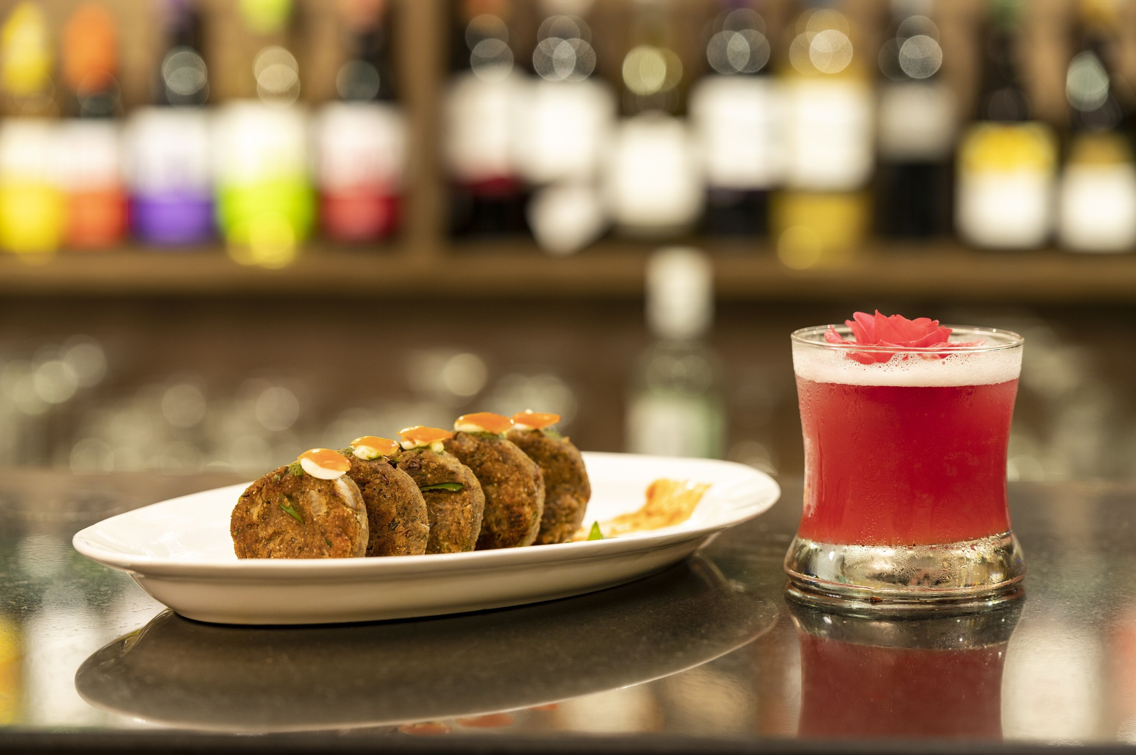 Un plato de falafel con guarniciones y un vaso de bebida roja con adorno sobre una barra.