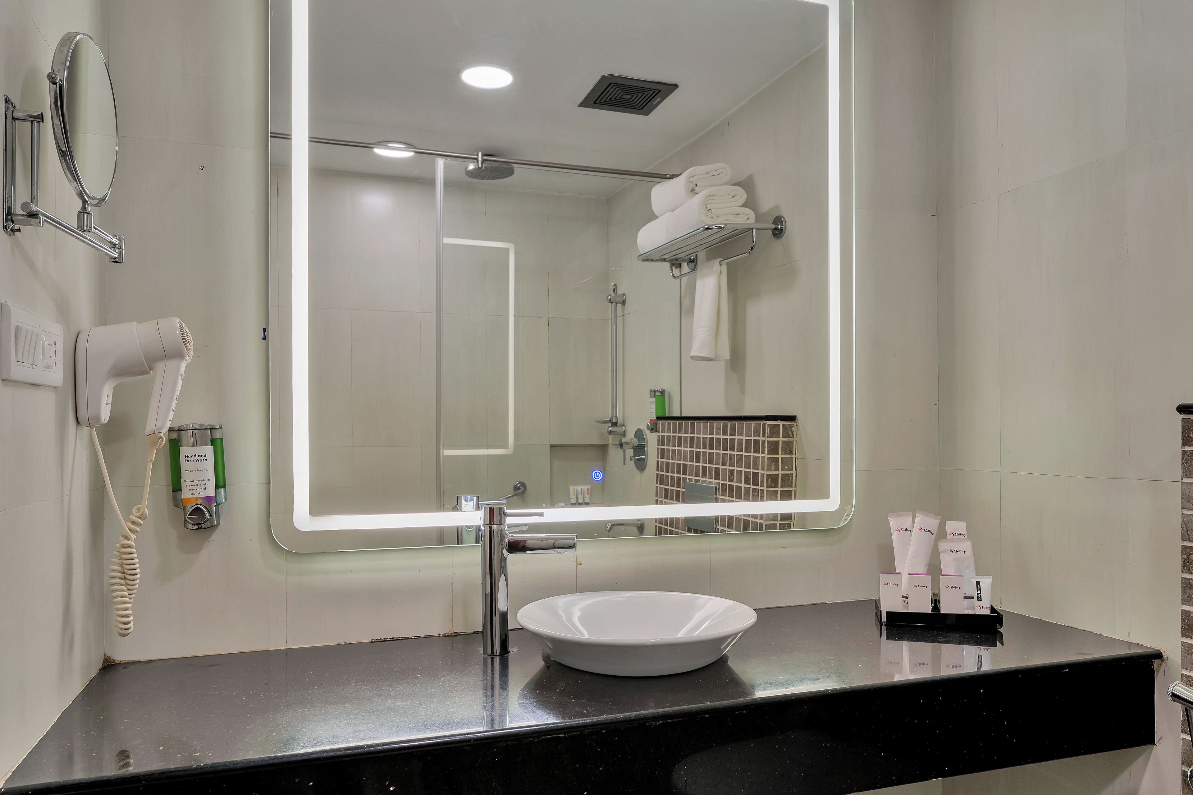 Un bagno moderno con uno specchio grande, un lavandino bianco, un asciugacapelli e un portascopevoli.
