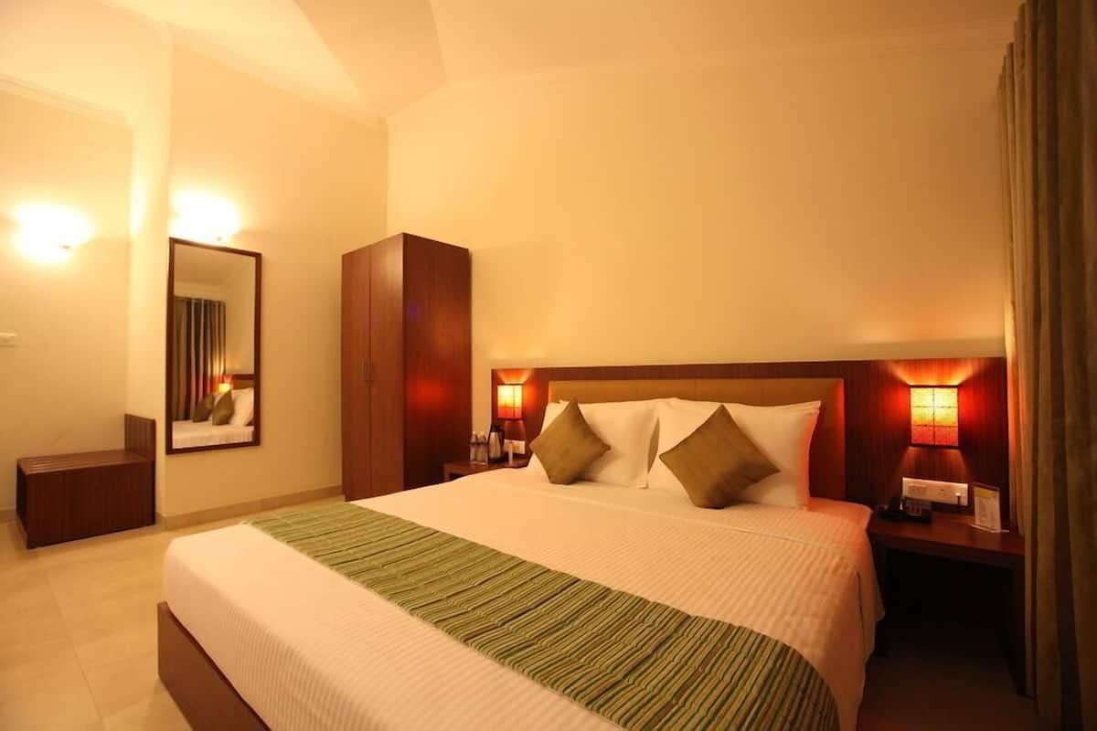 Une chambre d’hôtel avec un grand lit, une table de chevet avec une lampe, un miroir et une armoire en bois.