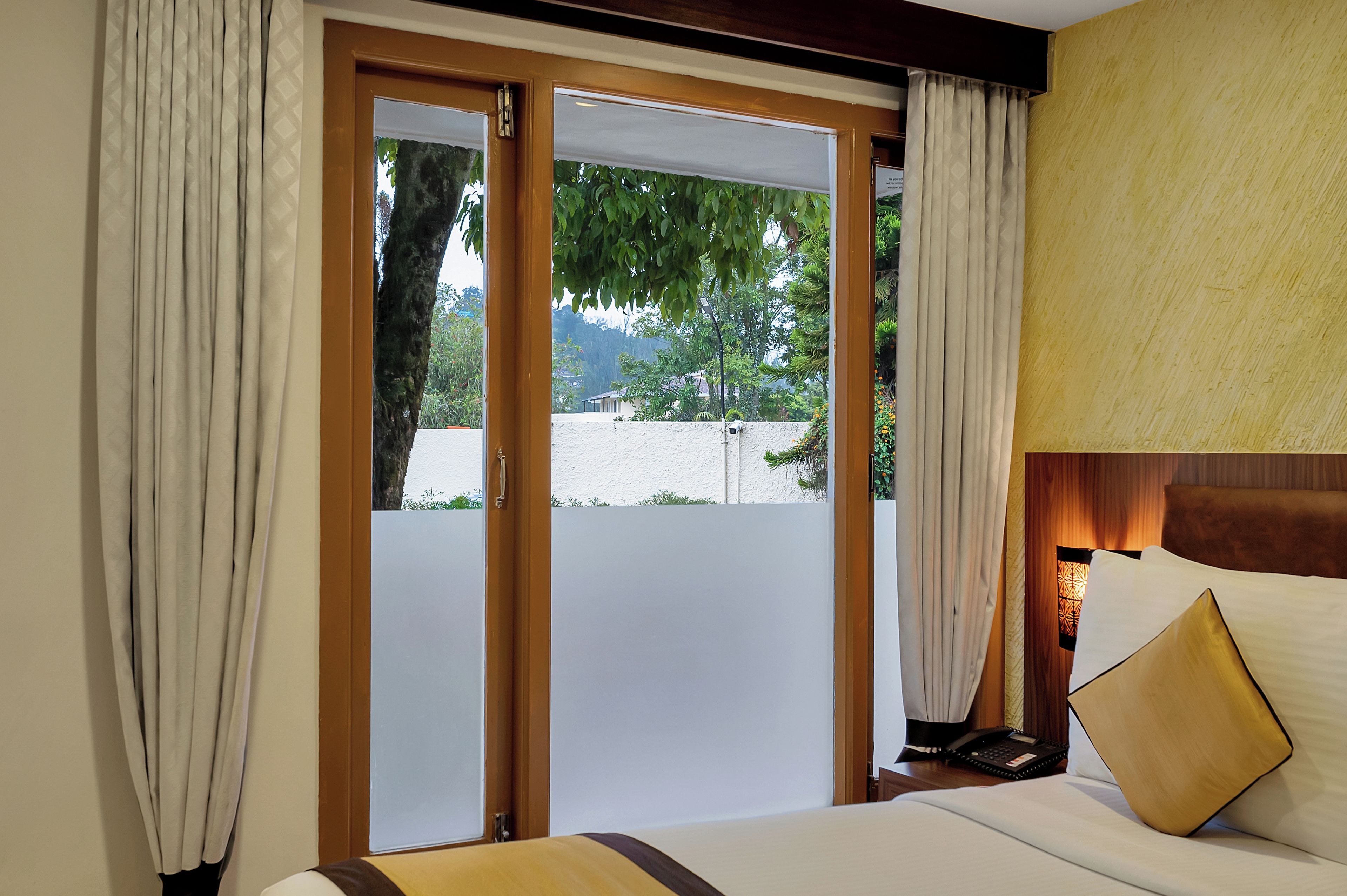 A hotel room with a bed, a bedside table, a lamp, and a view through a sliding door to the outdoors.