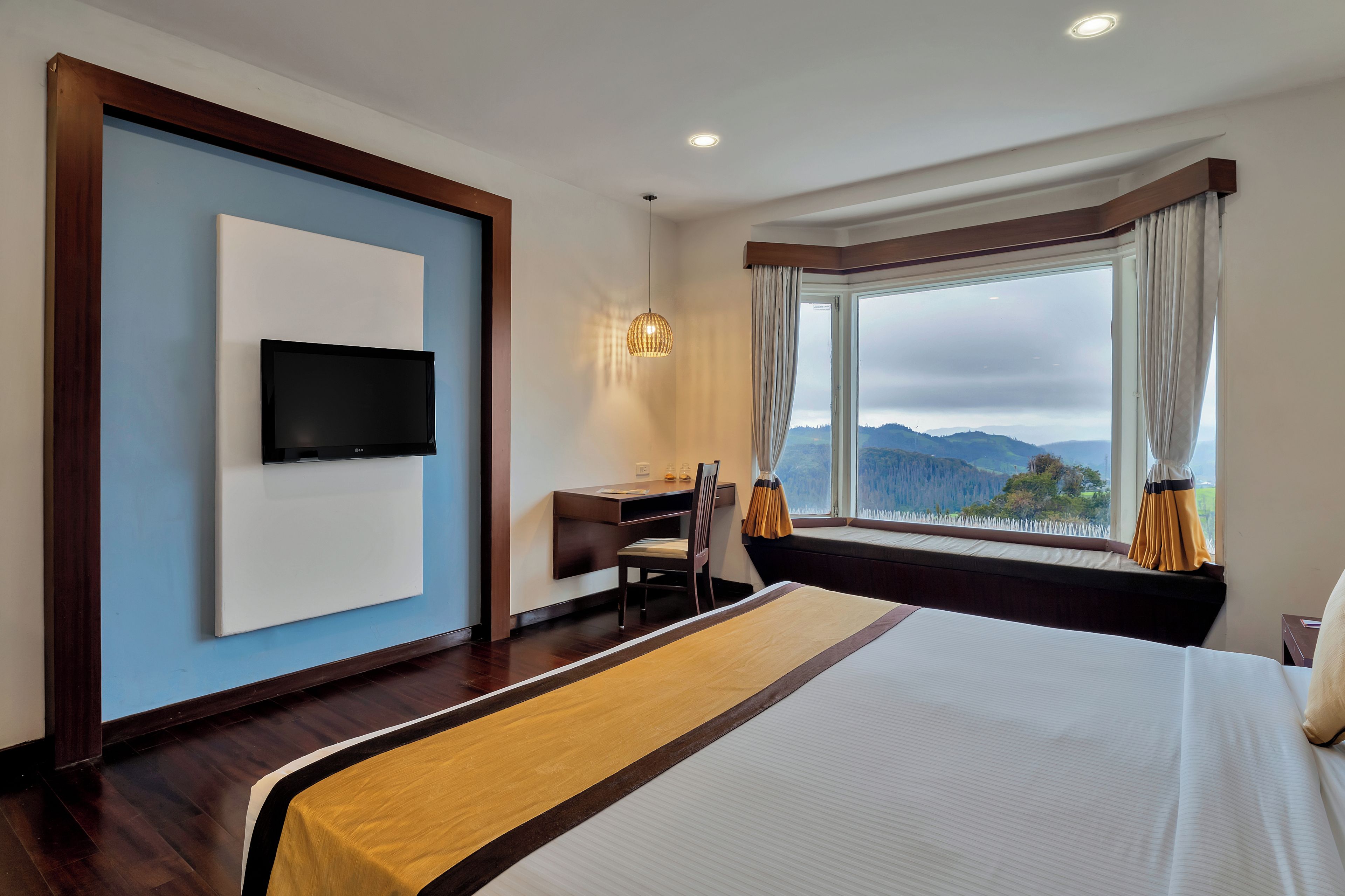 A hotel room with a bed, a desk, a chair, a TV, and a window with a view of the mountains.