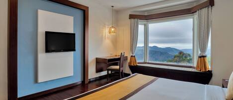 A hotel room with a bed, a desk, a chair, a TV, and a window with a view of the mountains.