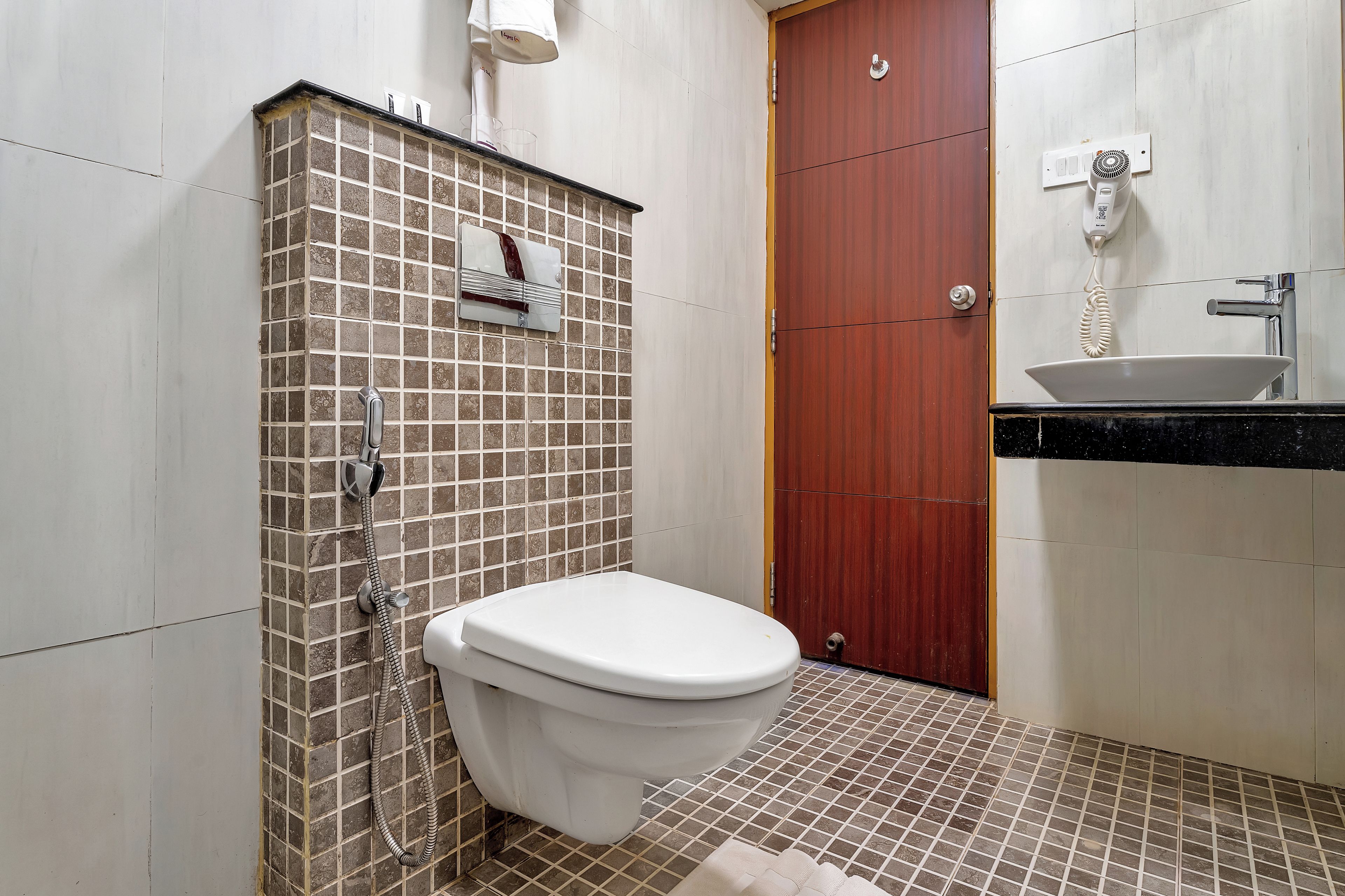 A bathroom with a white toilet, a shower area with a tiled wall, a wooden door, and a sink with a black countertop.